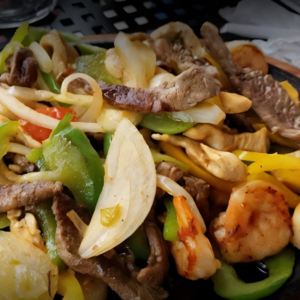 Close-up of sizzling fajitas with steak, shrimp, onions, and bell peppers on a dark plate.