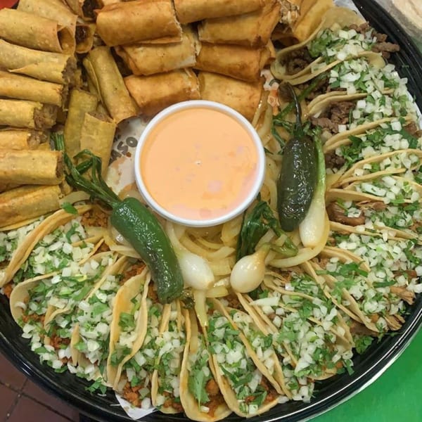 A large platter of El Paso Mexican Restaurant's taquitos and tacos with a side of dipping sauce.