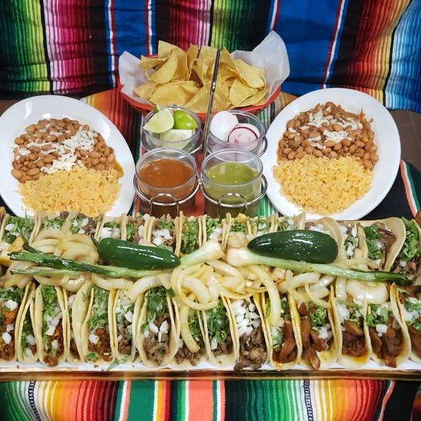 A vibrant spread of Mexican food, including tacos, rice, beans, chips, and salsas on a colorful striped blanket.