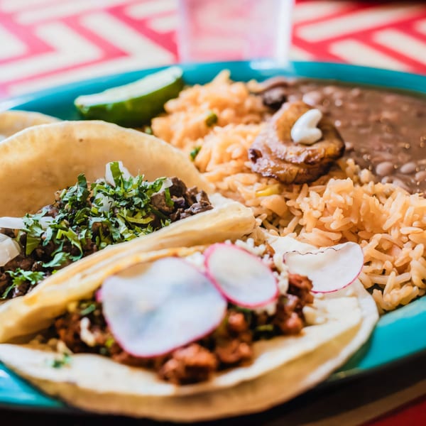 Two tacos with rice, beans, and plantains on a blue plate at El Paso Mexican Restaurant.