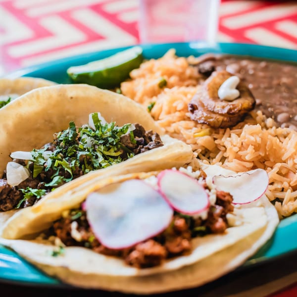 Two El Paso Mexican Restaurant tacos with rice, beans, and plantains on a blue plate.