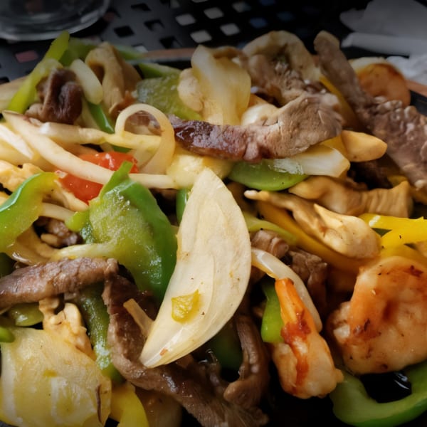 Close-up of sizzling fajitas with beef, shrimp, onions, and green bell peppers.