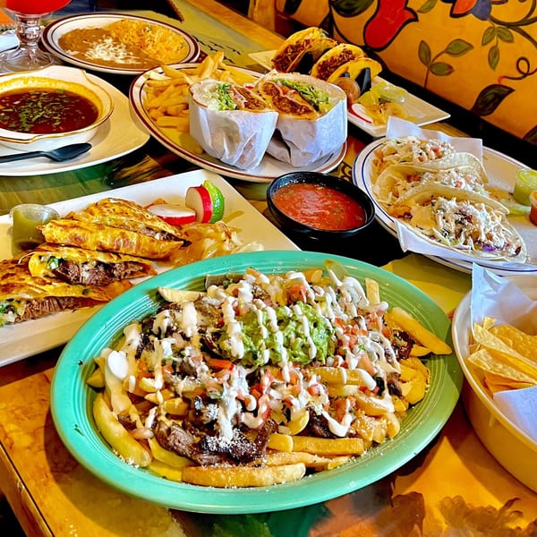 A table laden with various Mexican dishes, including tacos, burritos, quesadillas, and loaded fries.