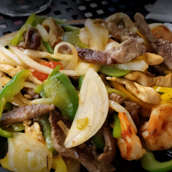 Close-up of sizzling fajitas with beef, shrimp, onions, and green bell peppers.