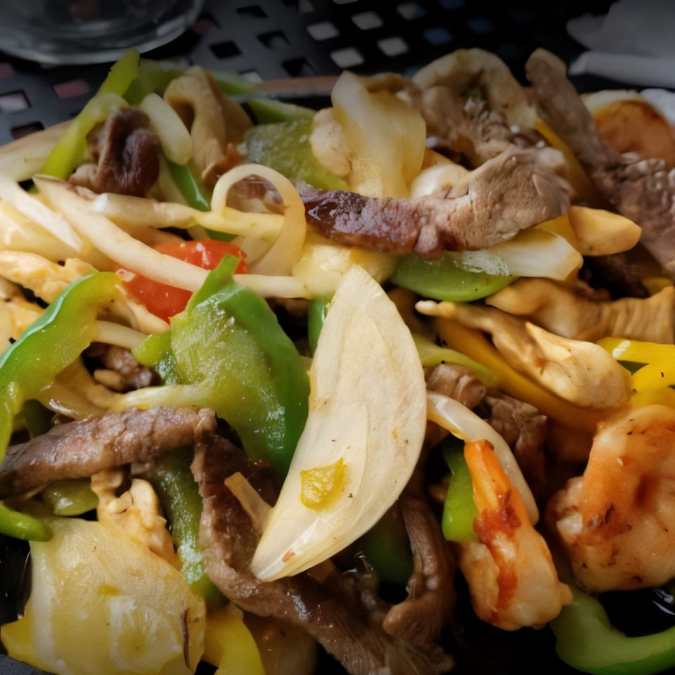Close-up of sizzling fajitas with beef, shrimp, onions, and green bell peppers.