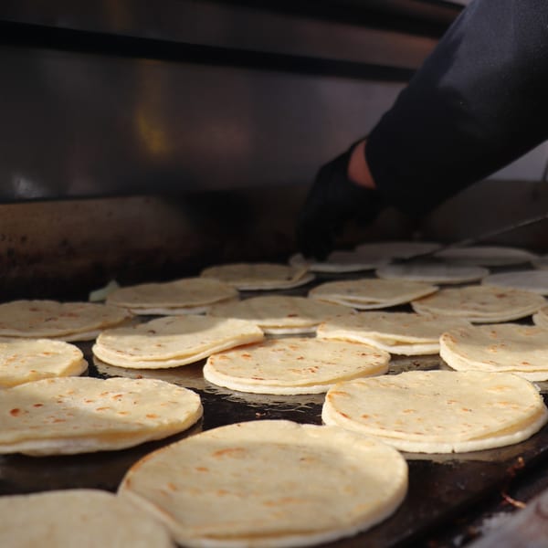 A person's hand flipping fresh tortillas on a large griddle at El Paso Mexican Restaurant.