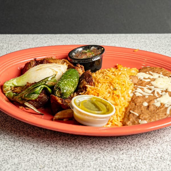 Mexican dish with grilled meat, onions, jalapeño, rice, refried beans, and two sauce cups on a red plate.