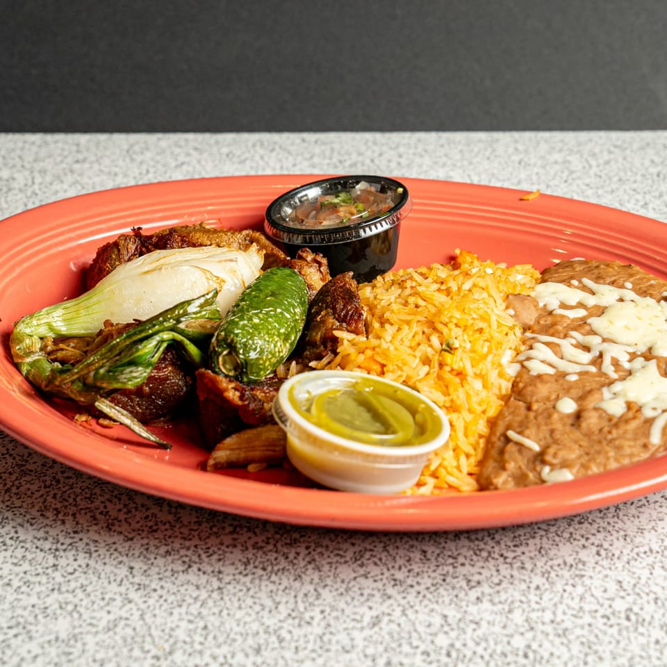 Mexican dish with grilled meat, onions, jalapeño, rice, refried beans, and two sauce cups on a red plate.