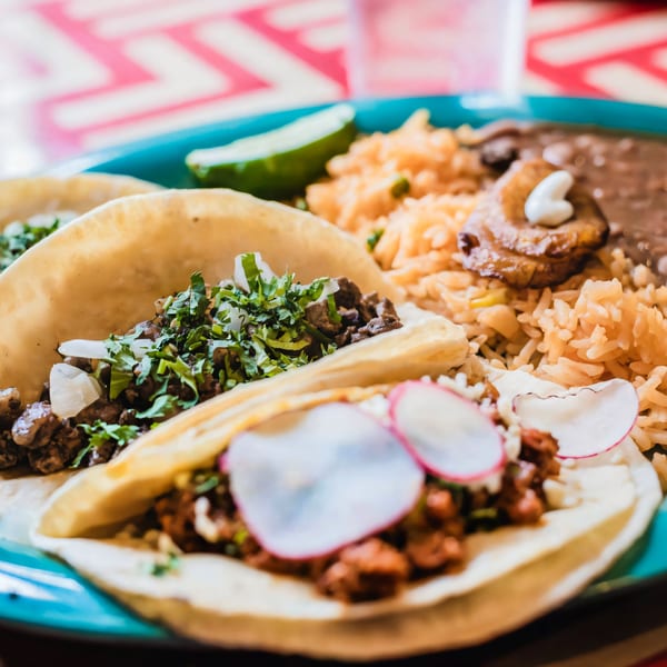 Two El Paso Mexican Restaurant tacos with rice, beans, and a lime wedge on a blue plate.